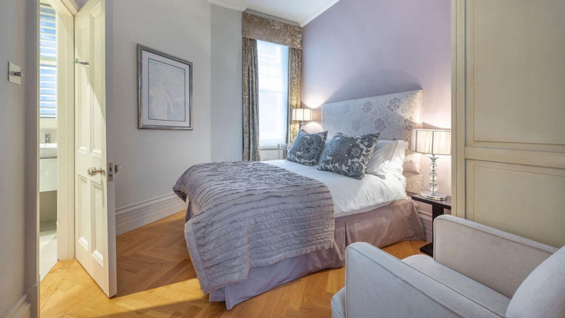 Bedroom with purple walls, curtains, tall upholstery, armchair, cabinets, wooden floor
