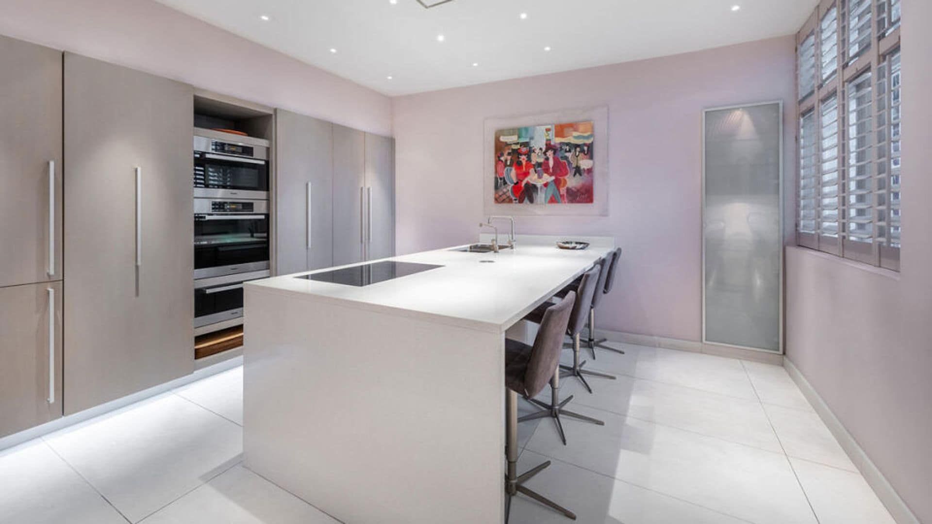 Kitchen with island, large wardrobe where appliances, high stools and pictures are hidden