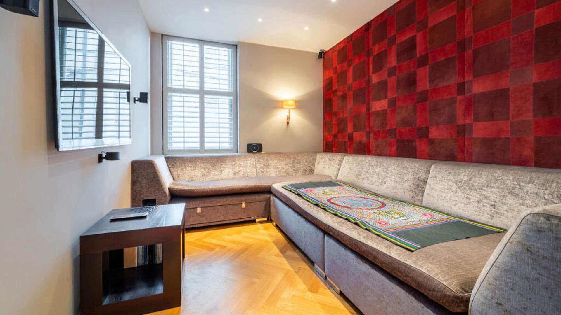TV ROOM WITH Gray corner sofa, red upholstered wall, television on the wall, auxiliary table and apply