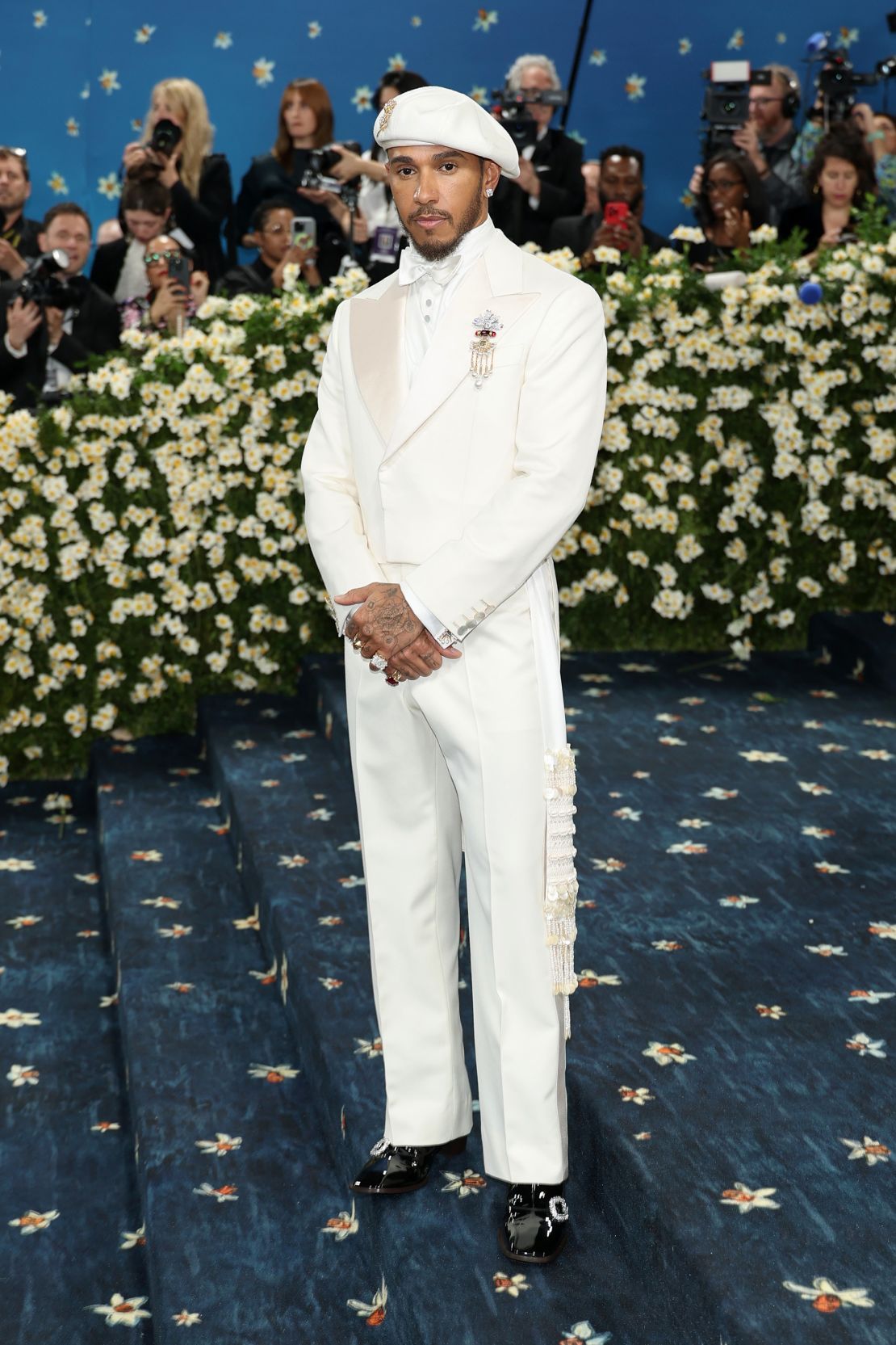 Met Gala co-chair Lewis Hamilton stunned in a custom white Wales Bonner tuxedo. “The color ivory denotes purity and status,” and “ancestral beads and freshwater pearls shine with garnet-colored diamonds… eternal amulets,” stylist Eric McNeal wrote on Instagram.