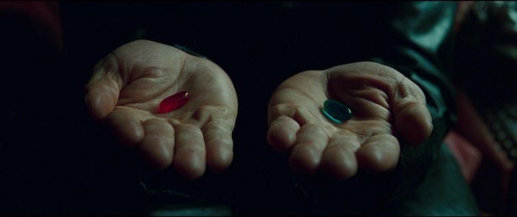 Two hands hold a red pill and another blue.